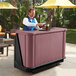 A man standing behind a Cambro mahogany portable bar with a drink.