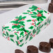 A 1/4 lb. holiday candy box with a holly pattern next to chocolates.