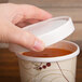 A person's hand holding a Solo Symphony paper soup cup with a red and white design and a vented paper lid.