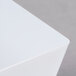 A close-up of a white square surface with a white plastic cube bowl on it.