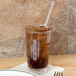 A Cambro clear plastic tumbler filled with brown liquid and ice with a straw.