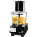 A Waring commercial food processor with a black batch bowl on a counter with sliced oranges on top.