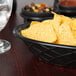 A charcoal oval weave polyethylene basket filled with chips on a table with a glass of water.