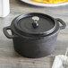 An American Metalcraft pre-seasoned black cast iron pot with a lid on a table.