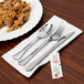 WNA Comet Reflections stainless steel look plastic fork, spoon, and napkin on a table.