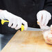 A person in white gloves using a Mercer yellow curved stiff boning knife to cut chicken.