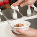 A person using a Carlisle pump condiment dispenser to pour brown liquid into a bowl of ice cream.