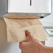 A hand pulling a Lavex Natural brown paper towel from a metal dispenser.