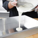 A person pouring white liquid into a Vollrath Wear-Ever aluminum cake pan.