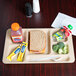 A beige Cambro 6 compartment tray with a sandwich, broccoli, and a bottle of juice on it.