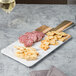 An Elite Global Solutions Sierra Faux Hickory Wood and Carrara Marble rectangular serving board with meat, cheese, and crackers on a table.