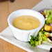 A plate of salad with a CAC Festiware bone white china ramekin of yellow dressing.