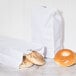 A bagel with a hole in the middle next to a 10 lb. white paper bag.