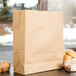A Duro natural kraft paper shopping bag on a table next to a plastic container of donuts.