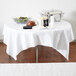 A table with a Hoffmaster white Linen-Like tablecloth and a bowl of salad.