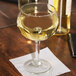 A Libbey Bolla Grande wine glass filled with white wine on a table with a napkin.