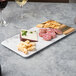 An Elite Global Solutions faux hickory wood and marble rectangular serving board with meat, cheese, and crackers on it.
