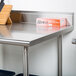 An Advance Tabco stainless steel work table with an undershelf and backsplash with a box on the counter.