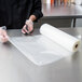 A person in a chef's uniform cutting a roll of ARY VacMaster full mesh plastic bags.