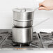 A hand holding a Vollrath stainless steel double boiler inset on top of a stove.