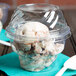 A clear plastic Fabri-Kal dome lid on a plastic cup of ice cream with a spoon.