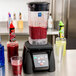 A Waring commercial blender with red liquid in it on a counter.