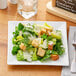 A plate of salad with croutons and parmesan cheese on an Acopa Bright White square porcelain plate.