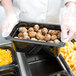 A person in gloves holding a black Cambro plastic food pan full of meatballs.