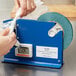 A person using a blue machine to cut Shurtape General Purpose Green Poly Bag Sealer Tape.