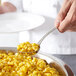 A person using a Thunder Group stainless steel serving ladle to scoop corn into a bowl.