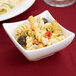 A bowl of pasta salad with olives and cheese in a white Arcoroc porcelain dish.