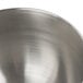 A close-up of a polished stainless steel KitchenAid mixing bowl with a handle.