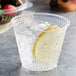 A clear Fabri-Kal Greenware plastic cup with ice and a lemon slice in it.