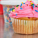 A Hoffmaster white fluted baking cup with a cupcake with pink frosting and sprinkles.