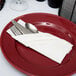 A red plate with a Hoffmaster FashnPoint white napkin and silverware on it.