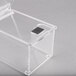 A clear plastic box with a black square on top.