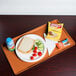 A Cambro citrus orange dietary tray with a sandwich, chips, and a drink on it.