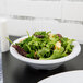 A Carlisle white rimmed melamine bowl filled with salad on a table.