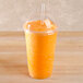 A Fabri-Kal Greenware plastic cup with a lid and straw filled with orange juice.