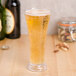 A close up of a customizable flared plastic pilsner glass filled with beer and bubbles on a table.