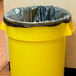 A yellow garbage can with a black Berry trash bag inside.
