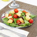 A Carlisle Petal Mist clear polycarbonate plate with a salad with tomatoes and croutons.
