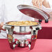 A chef using a Vollrath Maximillian round chafing dish to serve food.
