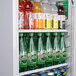 A Turbo Air white glass door refrigerator filled with sodas and cans.