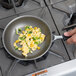 A hand using a Vollrath Wear-Ever aluminum non-stick frying pan to cook scrambled eggs with green peppers.
