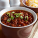 A bowl of Vanee chili with beans topped with cheese and green onions.
