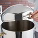 A person opening a Vollrath stainless steel coffee urn cover on a metal container.