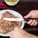 A hand holding a Mercer Culinary Genesis steak knife over a plate of meat.