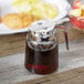 A Tablecraft glass syrup dispenser with a chrome lid on a table full of brunch items.