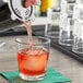 A person pouring a drink into an Anchor Hocking Clarisse old fashioned glass with ice.
